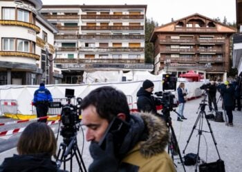 Δημοσιογράφοι στέκονται έξω από τα συντρίμμια του μοιραίου μπαρ, όπου τουλάχιστον 47 άνθρωποι βρήκαν τραγικό θάνατο και ορισμένες σοροί εξακολουθούν να βρίσκονται εκεί (φωτ.: EPA/Jean-Christophe Bott)