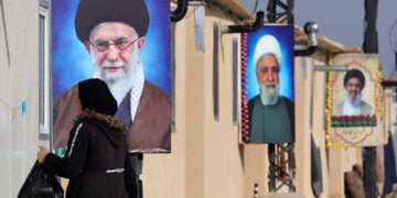 Πρόσφυγας περπατά μπροστά από πορτρέτα του αγιατολάχ Αλί Χαμενεΐ, του Ναΐμ Κάσεμ και του εκλιπόντος Χασάν Νασράλα στο συγκρότημα Ιμάμ Αλί, στο Χερμέλ της κοιλάδας Μπεκάα στην Υεμένη. 8 Ιανουαρίου 2026 (φωτ.: EPA / Wael Hamzeh)