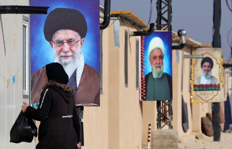 Πρόσφυγας περπατά μπροστά από πορτρέτα του αγιατολάχ Αλί Χαμενεΐ, του Ναΐμ Κάσεμ και του εκλιπόντος Χασάν Νασράλα στο συγκρότημα Ιμάμ Αλί, στο Χερμέλ της κοιλάδας Μπεκάα στην Υεμένη. 8 Ιανουαρίου 2026 (φωτ.: EPA / Wael Hamzeh)