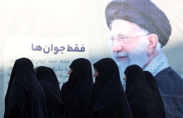 Ιρανές περνούν μπροστά από αφίσα του Αγιατολάχ Αλί Χαμενεΐ, κατά την άφιξή τους σε τελετή μνήμης για θύματα των αντικυβερνητικών διαδηλώσεων, στο τέμενος Μοσαλάχ της Τεχεράνης. 17 Φεβρουαρίου 2026 (φωτ.: EPA / Abedin Taherkenareh)