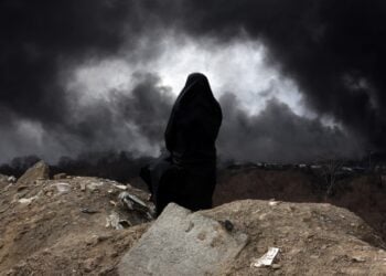 Ιρανή, μέλος της Ερυθράς Ημισελήνου κοιτά τον καπνό που βγαίνει από ιρανικό διυλιστήριο μετά από πλήγμα των ισραηλινών δυνάμεων (φωτ.: EPA/Abedin Taherkenareh)