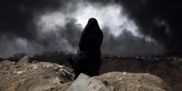 Ιρανή, μέλος της Ερυθράς Ημισελήνου κοιτά τον καπνό που βγαίνει από ιρανικό διυλιστήριο μετά από πλήγμα των ισραηλινών δυνάμεων (φωτ.: EPA/Abedin Taherkenareh)