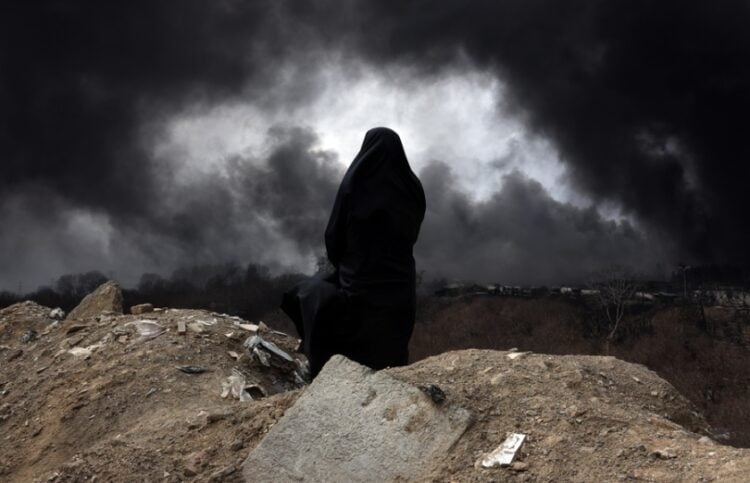 Ιρανή, μέλος της Ερυθράς Ημισελήνου κοιτά τον καπνό που βγαίνει από ιρανικό διυλιστήριο μετά από πλήγμα των ισραηλινών δυνάμεων (φωτ.: EPA/Abedin Taherkenareh)