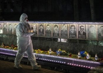 Ουκρανός, ντυμένος με τη στολή των εργαζομένων σε πυρηνικό σταθμό, κρατά κεριά σε τελετή μνήμης για τους «εκκαθαριστές» που έχασαν τη ζωή τους στις επιχειρήσεις καθαρισμού μετά την καταστροφή του Τσερνόμπιλ, στο Σλαβούτιτς της Ουκρανίας (φωτ.: EPA/MAKSYM KISHKA)