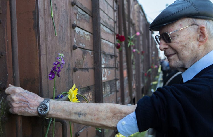 Ο Χάιντς Κούνιο το 2015, 72 χρόνια μετά τη θηριωδία, προτάσσει το χαραγμένο με τον αριθμό 109565 χέρι του μπροστά σε ένα από τα βαγόνια της ατμήλατης μηχανής Λβ 964, μία από αυτές που χρησιμοποιούσαν οι Ναζί για τα ταξίδια θανάτου προς το Άουσβιτς (φωτ.: ΑΠΕ-ΜΠΕ / Νίκος Αρβανιτίδης)