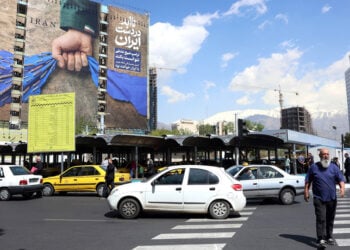 Ιρανός διασχίζει δρόμο μπροστά από γιγαντοαφίσα στην Τεχεράνη, με αναφορά στα Στενά του Ορμούζ και το σύνθημα «Για πάντα στο χέρι του Ιράν». 15 Απριλίου 2026 (φωτ.: EPA / Abedin Taherkenareh)