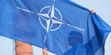 Καναδός στρατιωτικός της Πολυεθνικής Ταξιαρχίας του ΝΑΤΟ κρατά τη σημαία της Συμμαχίας κατά τη διάρκεια στρατιωτικής παρέλασης στο Αϊζκράουκλε της Λετονίας, στις 4 Μαΐου 2026 (φωτ.: EPA / Valda Kalnina)