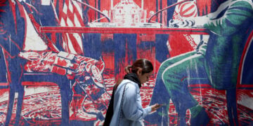 Μια νεαρή Ιρανή περνά μπροστά από αντι-αμερικανική τοιχογραφία με αναφορά στις διαπραγματεύσεις. Βρίσκεται κοντά στην πρώην αμερικανική πρεσβεία στην Τεχεράνη (φωτ.: EPA / Abedin Taherkenareh)