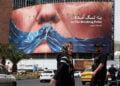 Ιρανοί περνούν δίπλα από μια τεράστια αντιαμερικανική πινακίδα που αναφέρεται στον Ντόναλντ Τραμπ και το Στενό του Ορμούζ στην πλατεία Βαλιάσρ, στην Τεχεράνη (φωτ.: EPA / Abedin Taherkenareh)