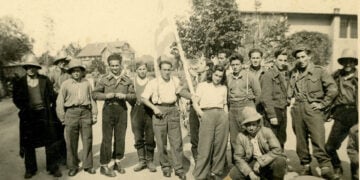 Ο Γιάννης Τζανίδης (κρατά την ελληνική σημαία) με συγκρατούμενούς του στο στρατόπεδο του Άουξμπουργκ τις πρώτες μέρες της απελευθέρωσης, Μάιος 1945 (πηγή: ΓΑΚ Μαγνησίας, Οικογενειακό Αρχείο Κωνσταντίνου Τζανίδη)