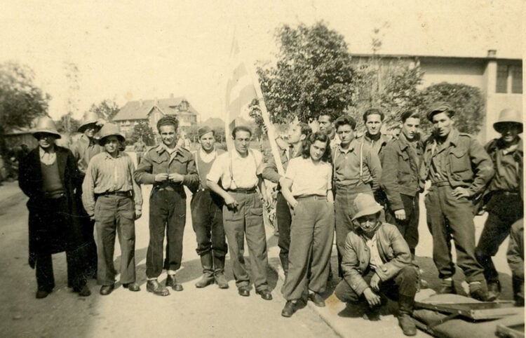 Ο Γιάννης Τζανίδης (κρατά την ελληνική σημαία) με συγκρατούμενούς του στο στρατόπεδο του Άουξμπουργκ τις πρώτες μέρες της απελευθέρωσης, Μάιος 1945 (πηγή: ΓΑΚ Μαγνησίας, Οικογενειακό Αρχείο Κωνσταντίνου Τζανίδη)