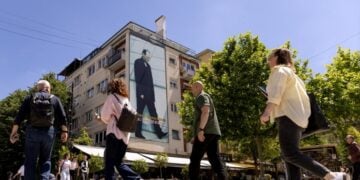 Άνθρωποι περπατούν στην κεντρική πλατεία μπροστά από μια φωτογραφία του πρώτου Προέδρου του Κοσόβου, Ιμπραήμ Ρουγκόβα, που είναι αναρτημένη σε κτήριο στην Πρίστινα, Κόσοβο (φωτ.: EPA/GEORGI LICOVSKI)