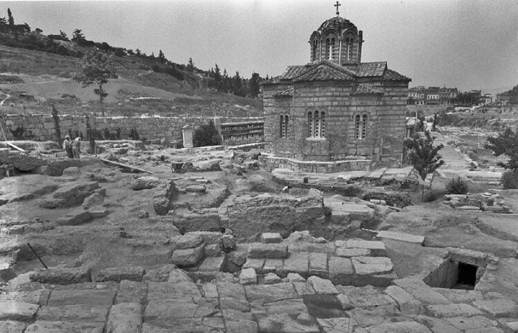 Σε πρώτο πλάνο η λιθόστρωτη Οδός των Παναθηναίων, στο κέντρο τα κατάλοιπα του υδρόμυλου και η λεκάνη απορροής όμβριων υδάτων (φωτ.: ΥΠΠΟ)