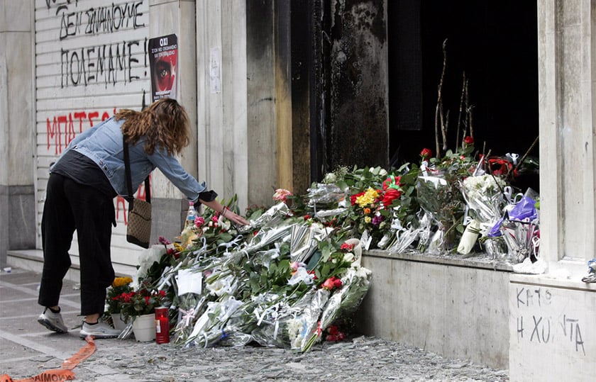 Γυναίκα αφήνει λουλούδια στο καμένο υποκατάστημα της Marfin στη Σταδίου, στη μνήμη των τριών εργαζομένων. Πέμπτη 6 Μαΐου 2010 (φωτ.: ΑΠΕ-ΜΠΕ / Παντελής Σαΐτας)
