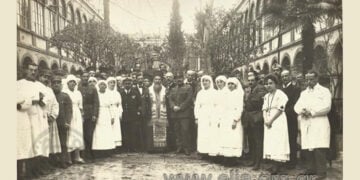 Ο μητροπολίτης Σμύρνης Χρυσόστομος κατά την τελετή των εγκαινίων των ιατρείων του Ερυθρού Σταυρού στο Γραικικό Νοσοκομείο Σμύρνης «Άγιος Χαράλαμπος». Δίπλα του ο πλοίαρχος Η. Μαυρούδης και ο αρχίατρος Β. Τσουνούκας (πηγή: Φωτογραφικό Αρχείο ΕΛΙΑ)