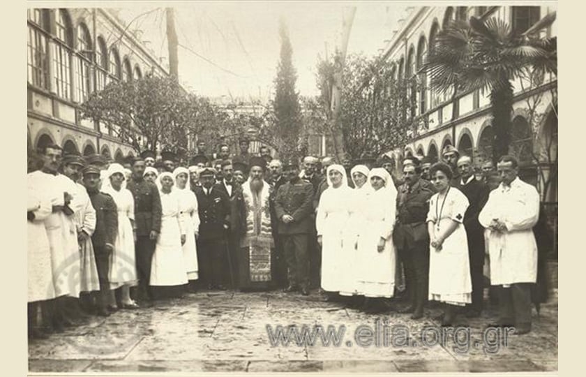 Ο μητροπολίτης Σμύρνης Χρυσόστομος κατά την τελετή των εγκαινίων των ιατρείων του Ερυθρού Σταυρού στο Γραικικό Νοσοκομείο Σμύρνης «Άγιος Χαράλαμπος». Δίπλα του ο πλοίαρχος Η. Μαυρούδης και ο αρχίατρος Β. Τσουνούκας (πηγή: Φωτογραφικό Αρχείο ΕΛΙΑ)