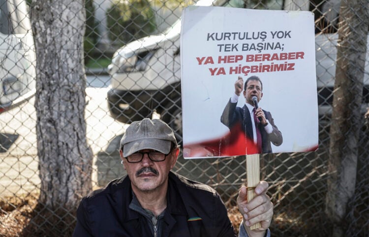 Υποστηρικτής του φυλακισμένου δημάρχου Κωνσταντινούπολης Εκρέμ Ιμάμογλου κρατά πλακάτ με το σύνθημα «Δεν υπάρχει σωτηρία για κανέναν μόνο του – ή όλοι μαζί ή κανείς», έξω από τις φυλακές Μαρμαρά στην Κωνσταντινούπολη. 15 Ιανουαρίου 2026 (φωτ.: EPA / Erdem Sahin)