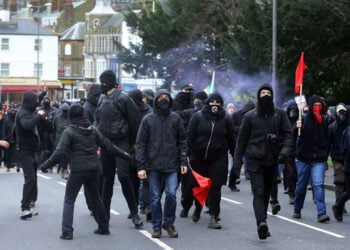 Κουκουλοφόροι διαδηλωτές στον σιδηροδρομικό σταθμό Dover Priory, καθώς αποχωρούν από το Ντόβερ μετά τον πολύωρο αποκλεισμό των οδών προς το λιμάνι. Σάββατο 5 Σεπτεμβρίου 2026 (φωτ.: Oscar Rihll / PA Wire / DPA / Picture Alliance)