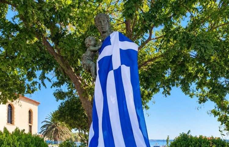 Το Μνημείο της Μικρασιάτισσας Μάνας στη Νέα Κούταλη, καλυμμένο με την ελληνική σημαία μετά την επιμνημόσυνη δέηση και την κατάθεση στεφάνων (φωτ.: Facebook / Κοινότητα Νέας Κούταλης Λήμνου)