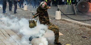 Διαδηλωτής κλωτσάει δακρυγόνο κατά τη διάρκεια συγκρούσεων με την αστυνομία σε διαμαρτυρία ενάντια στο αυξανόμενο κόστος διαβίωσης και τις περικοπές στις δημόσιες υπηρεσίες στο Παρίσι, Γαλλία (φωτ.: EPA/ MOHAMMED BADRA)