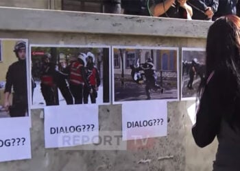 Διαδηλώτρια τοιχοκολλάει φωτογραφίες έξω από το γραφείο του Έντι Ράμα. Η λέξη «διάλογος» συνοδεύει τα αποδεικτικά στοιχεία για την αστυνομική βία. Τρίτη 20 Οκτωβρίου 2026 (πηγή: YouTube / Report TV)