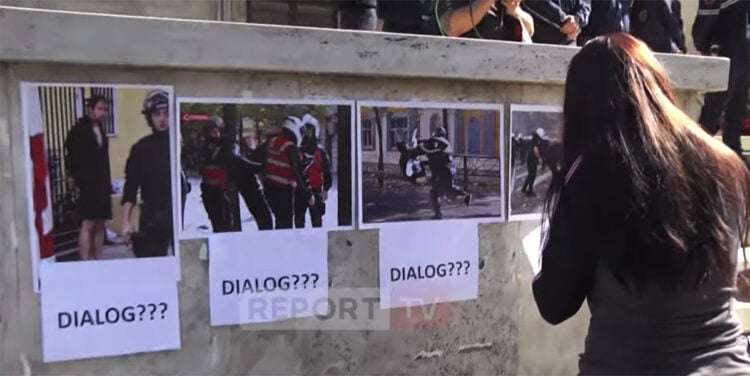 Διαδηλώτρια τοιχοκολλάει φωτογραφίες έξω από το γραφείο του Έντι Ράμα. Η λέξη «διάλογος» συνοδεύει τα αποδεικτικά στοιχεία για την αστυνομική βία. Τρίτη 20 Οκτωβρίου 2026 (πηγή: YouTube / Report TV)