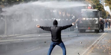 Διαδηλωτής με πέτρες στα χέρια απέναντι από «Αύρα», κατά τη διάρκεια φοιτητικής διαδήλωσης στα Τίρανα, στις 15 Οκτωβρίου 2026 (φωτ.: EPA / Malton Dibra)