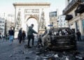 Περαστικοί μπροστά σε καμένο αυτοκίνητο στο Παρίσι, στις 18 Οκτωβρίου 2026, μετά τις συγκρούσεις μεταξύ αστυνομικών και διαδηλωτών στη διάρκεια των πανεθνικών κινητοποιήσεων κατά του υψηλού κόστους διαβίωσης (φωτ.: EPA / Mohammed Badra)
