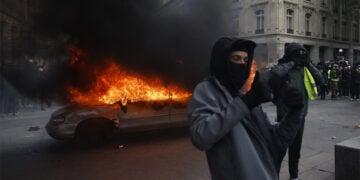 Διαδηλωτές ποζάρουν μπροστά σε φλεγόμενο αυτοκίνητο στο Παρίσι, στη διάρκεια διαδήλωσης κατά της ακρίβειας και των περικοπών στις δημόσιες υπηρεσίες, στις 17 Οκτωβρίου 2026 (φωτ.: EPA / Mohammed Badra)